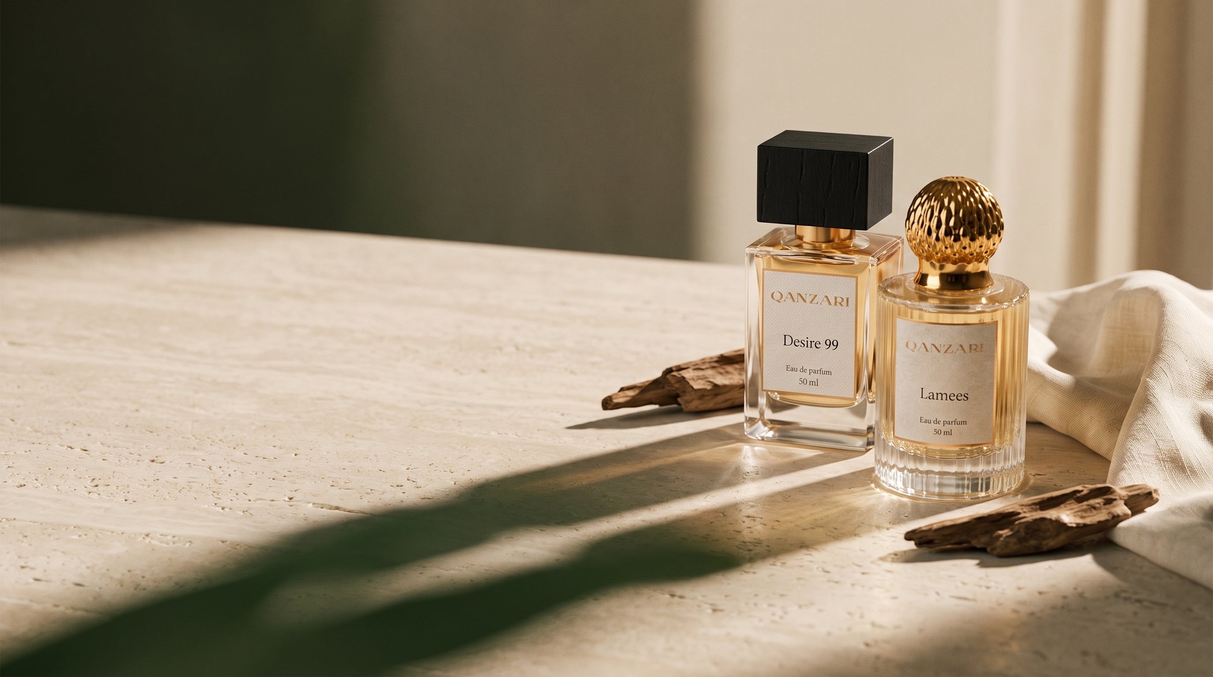 Qanzari Desire 99 and Lamees 50ml bottles on pale stone with oud wood and linen in warm evening light